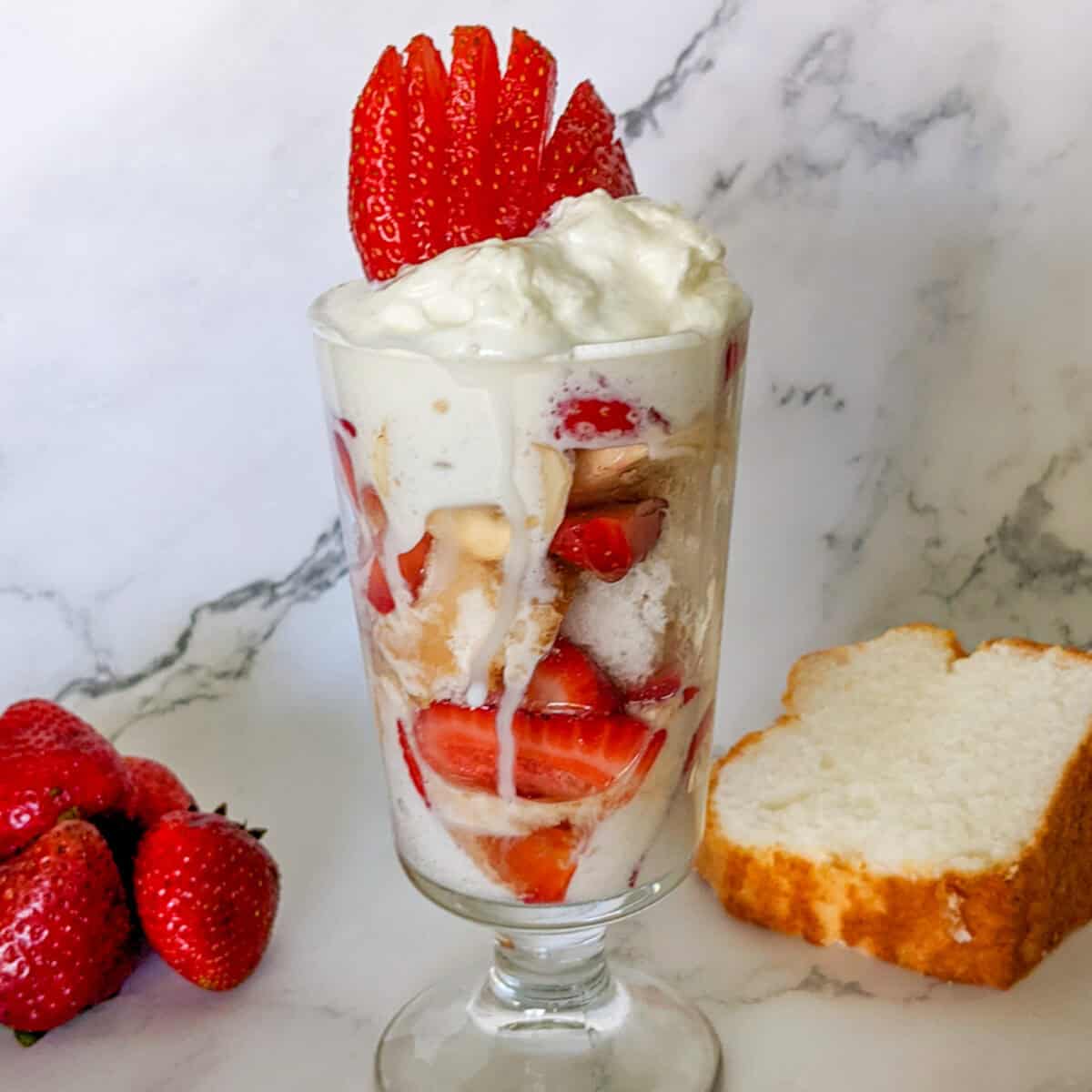 Colorful strawberry and sponge cake parfait layered with whipped cream in a glass cup.